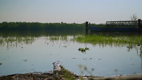 un barco abandonado al borde de la orilla de un canal tranquilo por la mañana