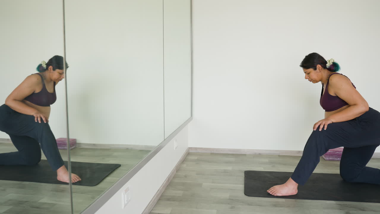 Mulher indiana faz exercícios de mobilidade de yoga em frente ao espelho da academia no terceiro trimestre de gravidez.