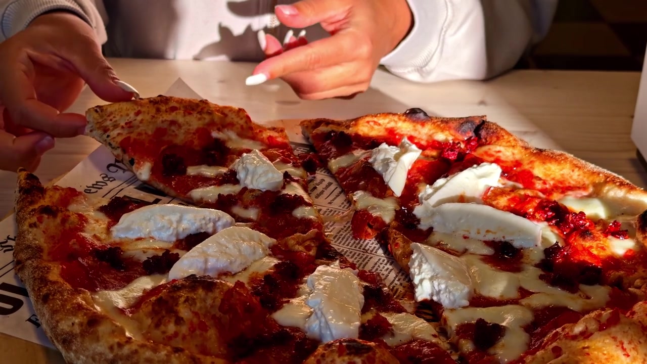 Mani di donna che afferrano una pizza appena sfornata, condita con salsa di pomodoro, formaggio fuso e ciuffi di ricotta, che catturano la calda atmosfera della cucina italiana e il cibo invitante di un ristorante.