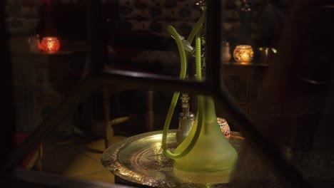vista cercana desde el exterior de un salón de té árabe con reflejos de luz en la noche, velas y narguiles