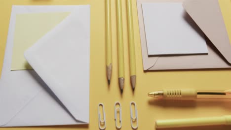 Close-up-of-pens,-pencils-and-stationery-arranged-on-yellow-background,-in-slow-motion