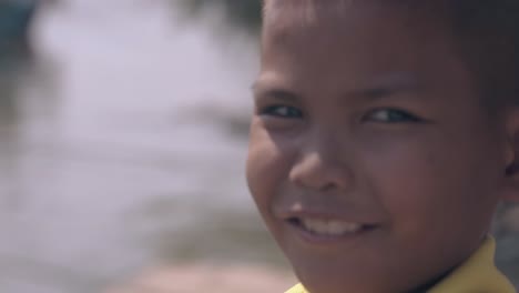 Asian-boy-smiles-to-camera-against-blurred-harbor-on-day