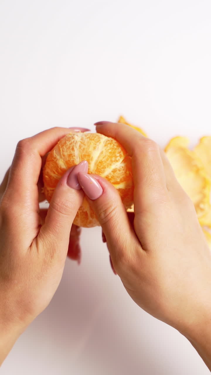 Process of clearance the mandarin. Female's hands cleaning an orange fresh fruit on white background. Top view. Vertical video