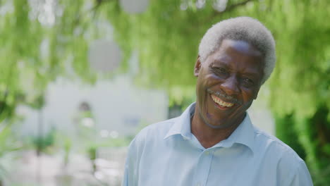 Portrait-Of-Relaxed-Senior-Man-Standing-In-Garden-At-Home-After-Retirement