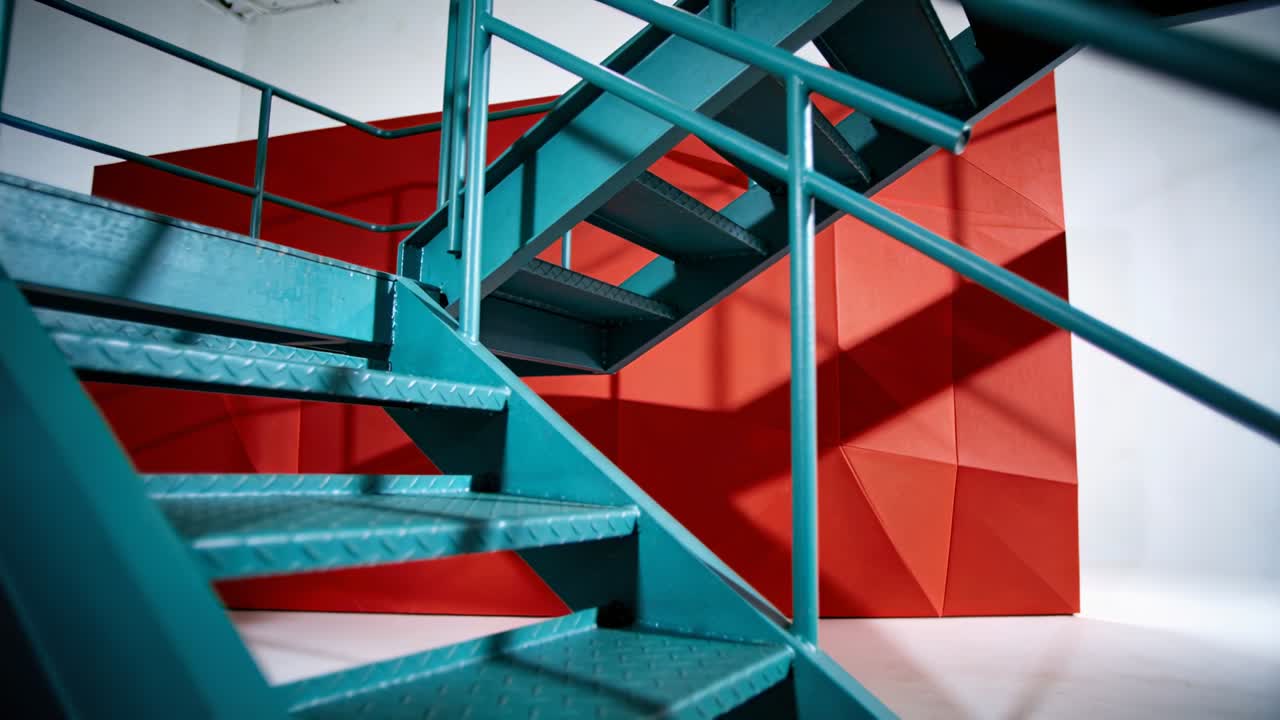 Telecamera che si muove verso l'alto mentre le luci proiettano ombre diagonali su un pannello rosso, rivelando scale color verde acqua.