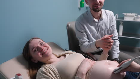 pregnant woman having ultrasound scan at the gynecologist office while loving husband holding her hand 6