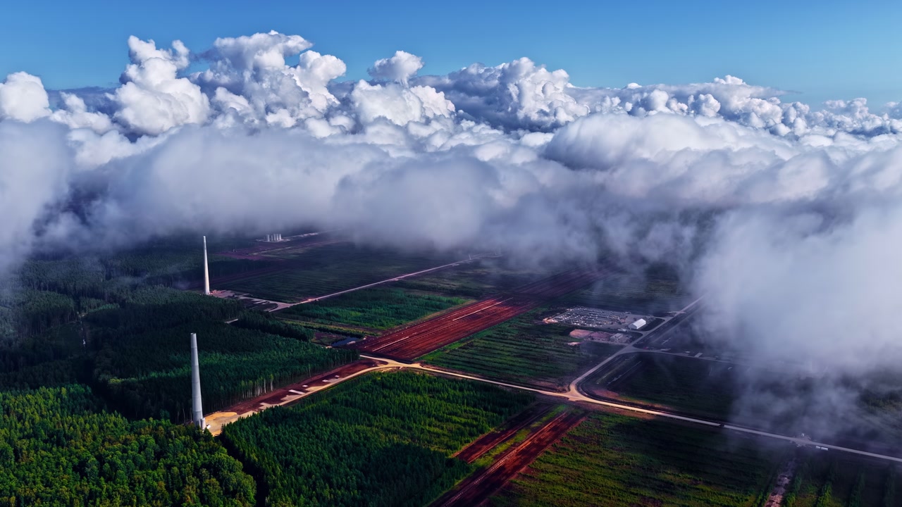 Striking aerial view of a landscape partly covered in low-hanging clouds. It showcases combination of structured farmland, scattered industry, and rolling clouds.