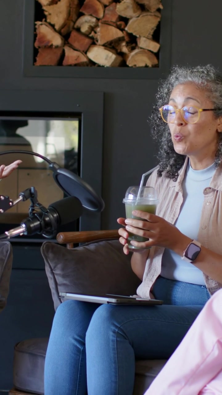 Video verticale: Una donna in rosa che parla e sorseggia una bevanda verde sul divano, la telecamera si allarga, il microfono cattura l'audio.