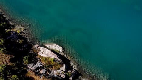 Aerial-flyover-over-tiny-islands-in-the-waters-of-Lac-de-Salanfe-in-Valais,-Switzerland-on-a-sunny-autumn-day-in-the-Swiss-Alps-with-a-pan-up-view-to-surrounding-alpine-peaks-and-cliffs