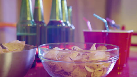 primer plano de papas fritas, botellas de cerveza y vasos de plástico en una mesa de fiesta en casa