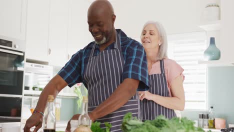 Happy-senior-diverse-couple-wearing-aprons-in-kitchen