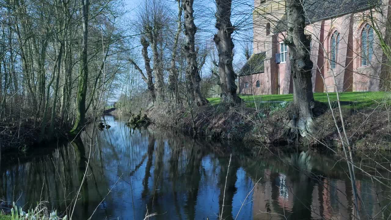 Fredelig kanal med spejlinger af træer og historisk murstenskirke