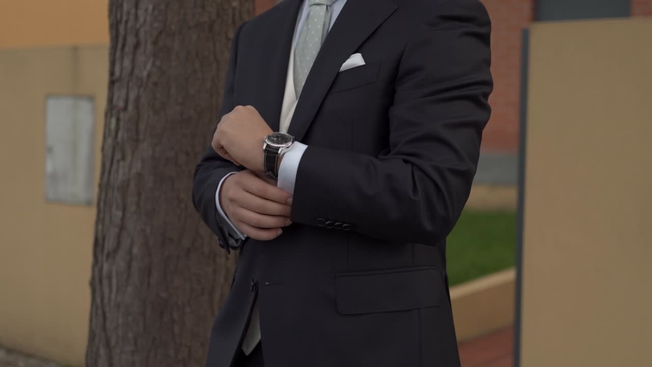 Groom in dark suit adjusting silver watch showcasing elegance and preparation