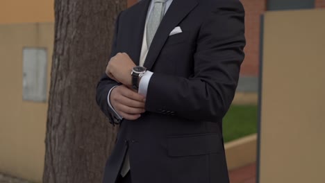 Groom in dark suit adjusting silver watch showcasing elegance and preparation