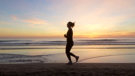 Frau-Läuft-Am-Strand-Entlang-Mit-Wunderschönem-Sonnenaufgangslicht