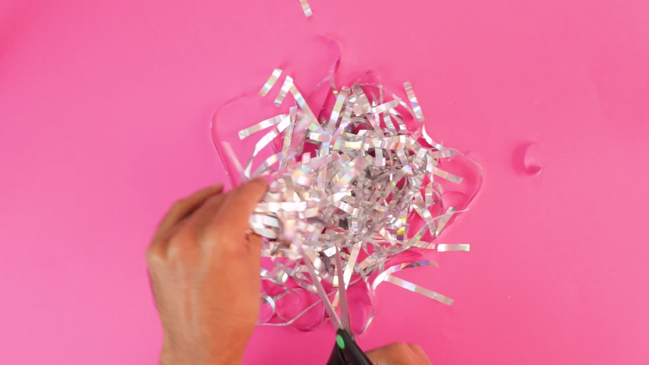 Cutting iridescent paper strips into silver confetti with scissors