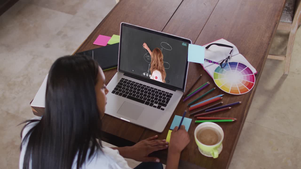 Estudiante caucásica usando una laptop en videollamada con una profesora, tomando apuntes.