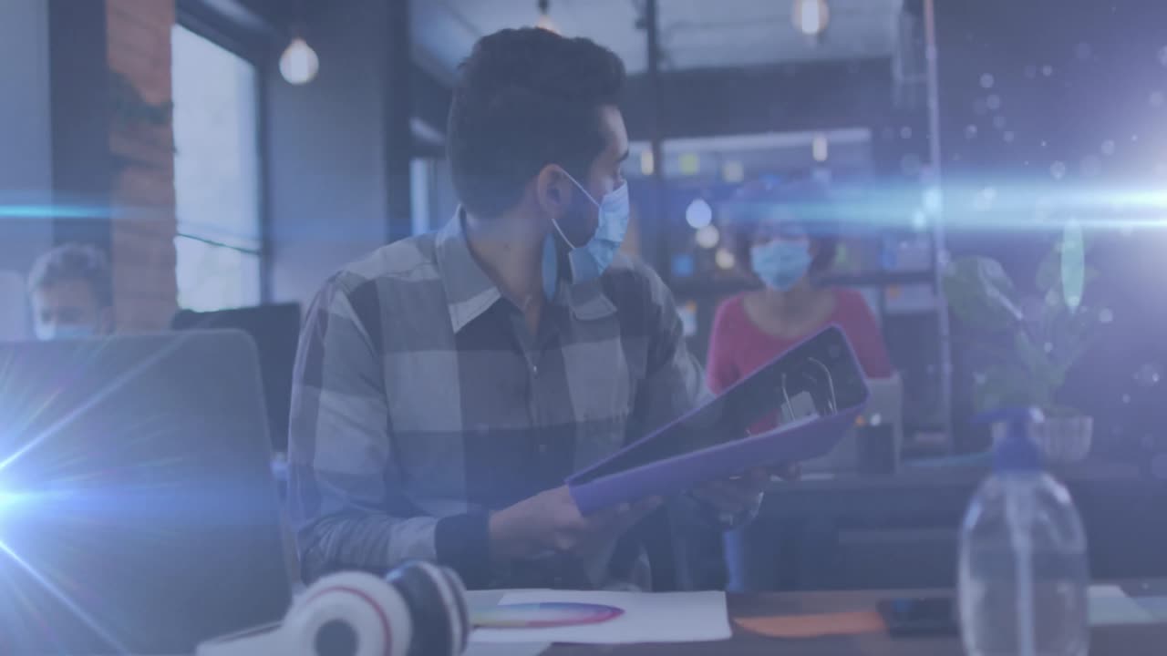 Spots of light against man wearing face mask passing the file to his female colleague at office