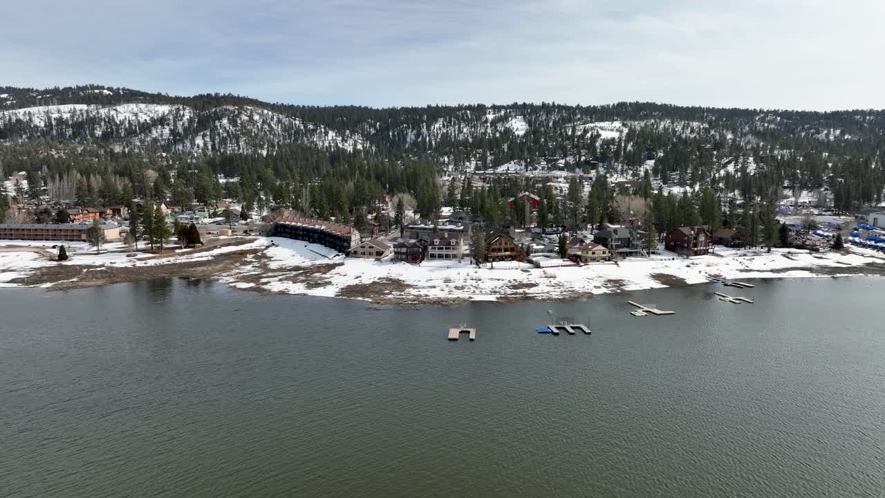 vista frontal de los hoteles del lago con montañas, bosques de nieve y algunos edificios en big bear mountain ca.