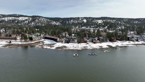 Vista-Frontal-De-Los-Hoteles-Del-Lago-Con-Montañas,-Bosques-Nevados-Y-Algunos-Edificios-En-Big-Bear-Mountain-Ca.