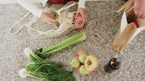 midsection of caucasian couple unpacking grocery shopping together in kitchen, slow motion