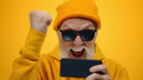 aged man gesticulating indoors. happy guy playing on cellphone in studio.