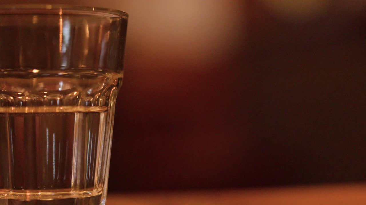 Acqua gassata trasparente versata in un bicchiere, con formazione di bolle su uno sfondo sfocato e caldo da pub