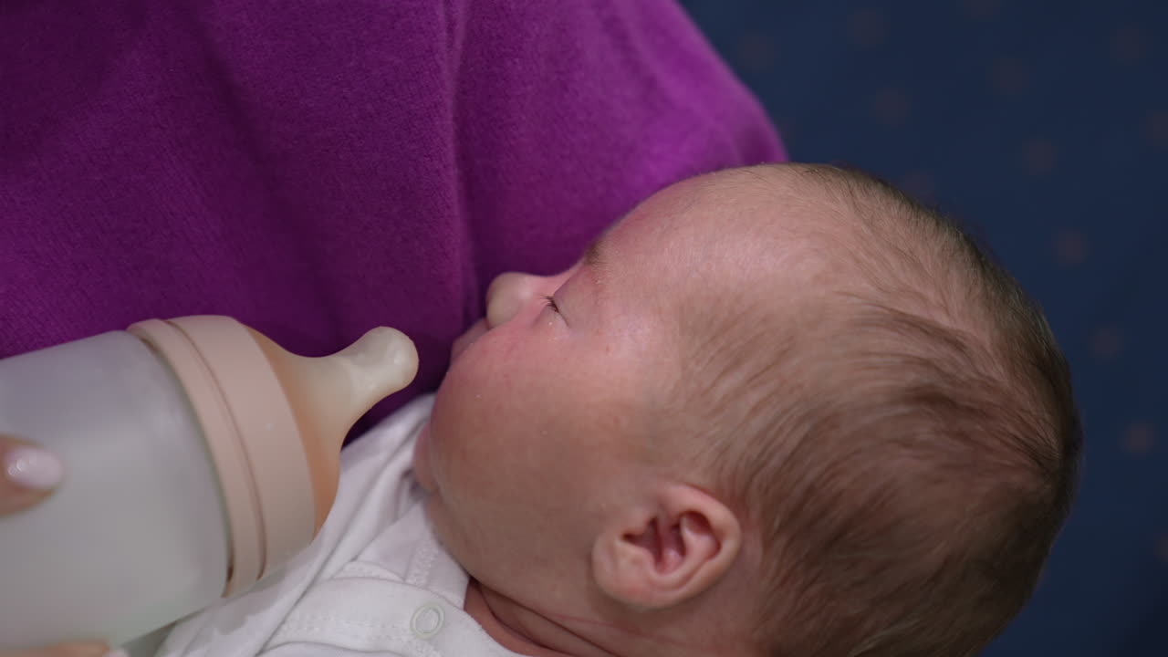 Cute little baby is hungry and opening its mouth ready to eat. Caring mother gives baby a bottle. Baby takes the milk bottle.