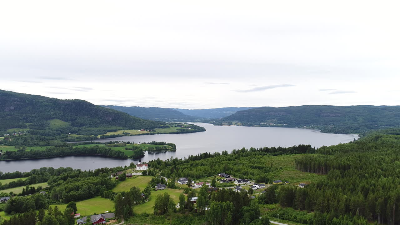 un dron captura un lago tranquilo rodeado de vegetación, colinas y casas rurales en noruega.