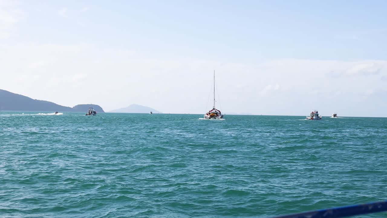 푸켓의 푸르키즈 바다를 가로질러 항해하는 요트, 은 하늘 아래 울창한 섬들에 둘러싸여, 조용한 해상 여행을 포착합니다.