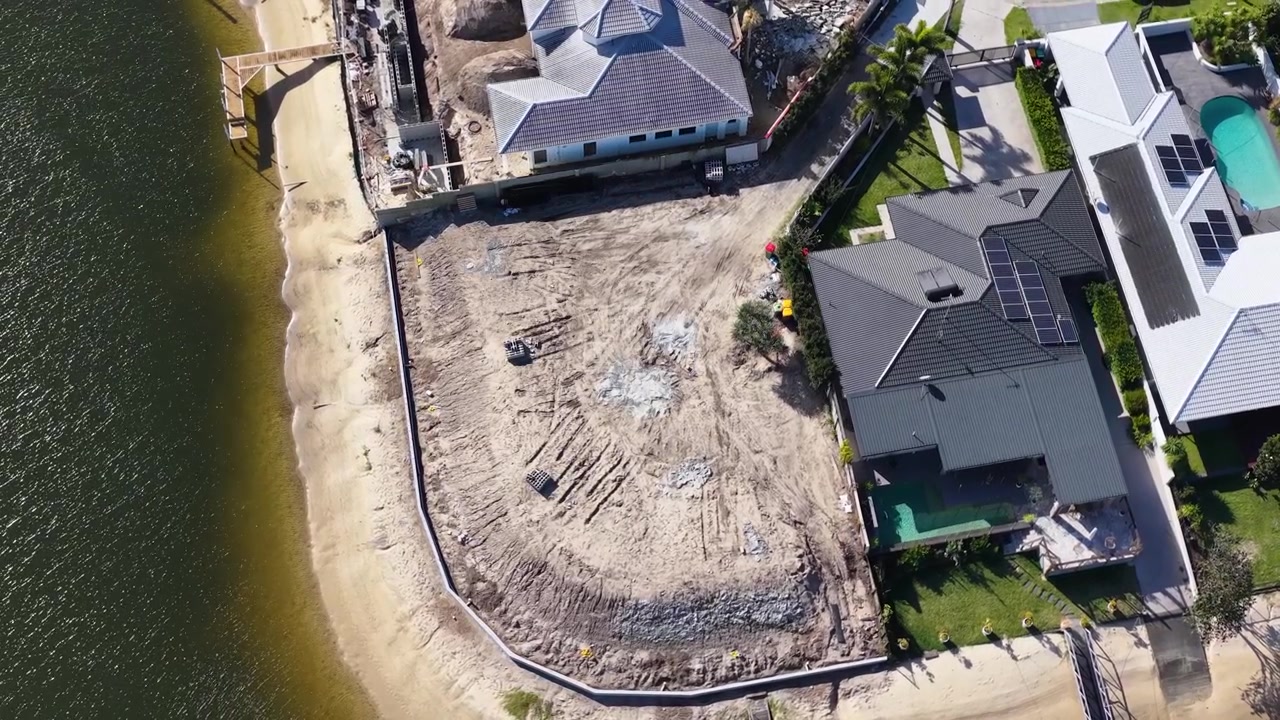 High-angle drone shot reveals residential development progress along a sunny coastal canal waterway.