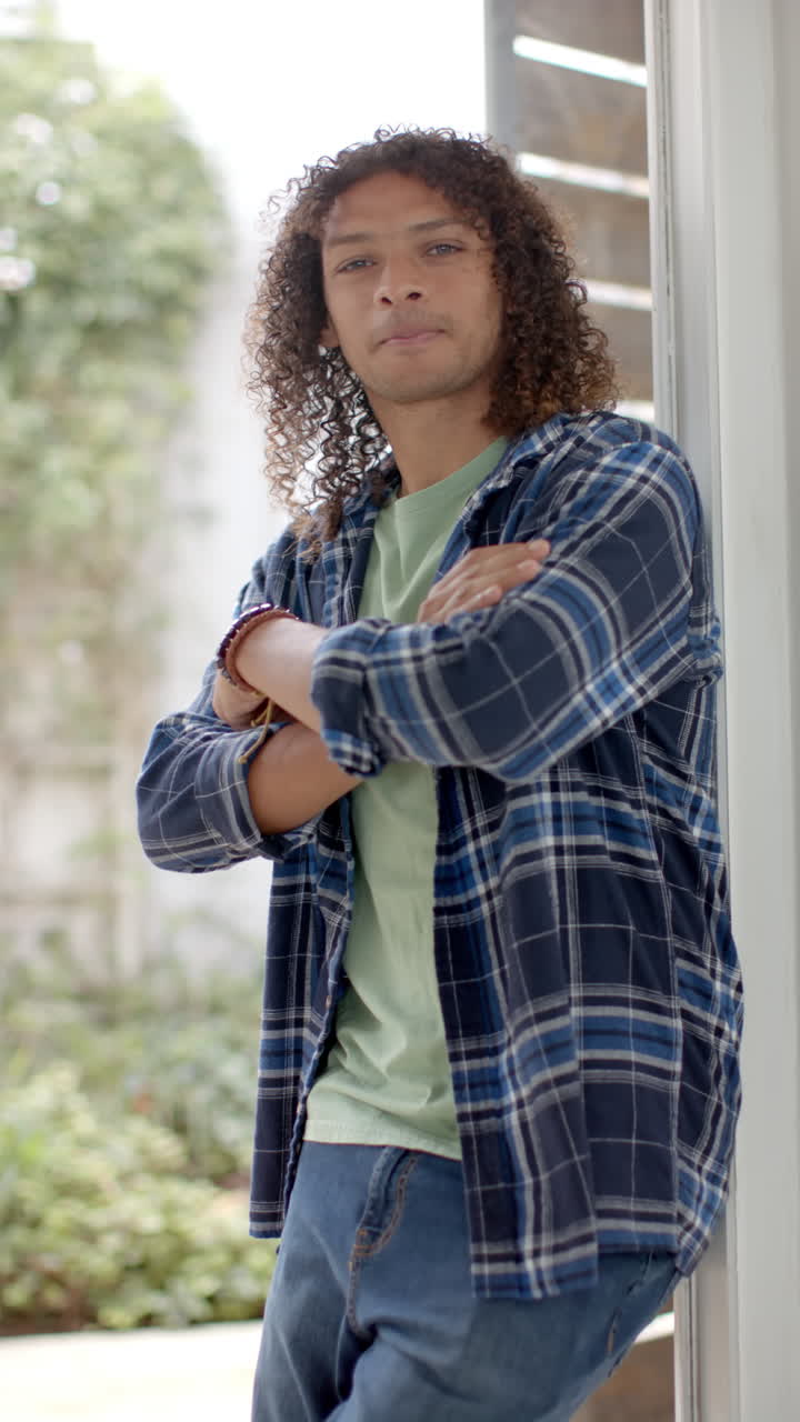 Vertical video of portrait of biracial man with long curly hair at home, slow motion