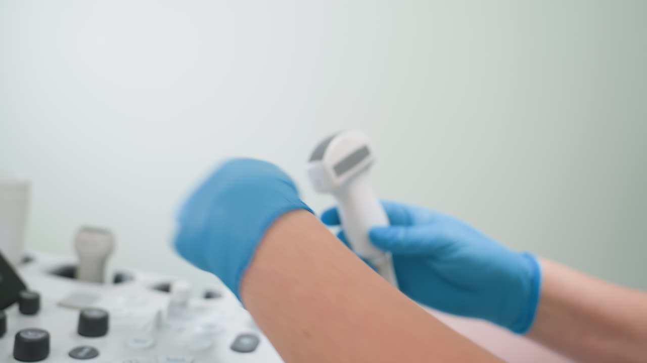 Female clinician wearing lab gloves carefully removes transducer from holder in preparation for applying gel, preparing for patient examination in clinical environment with medical equipment