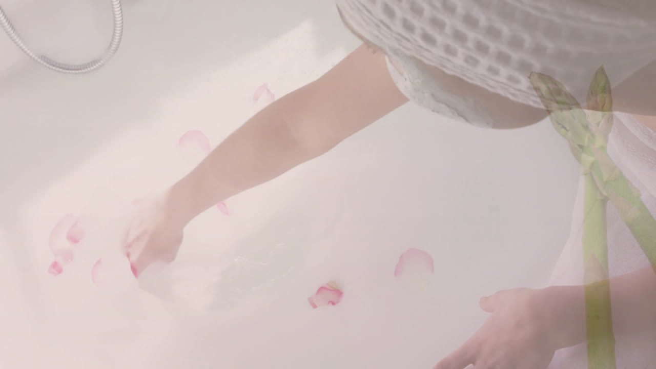 Reaching into bathtub with floating pink petals, person wearing white clothing