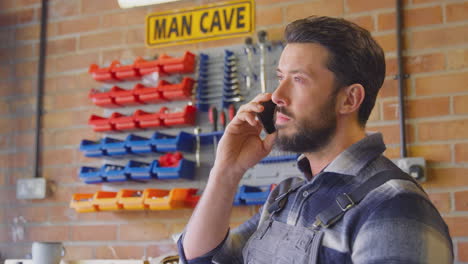 man wearing overalls in garage workshop at home talking on mobile phone