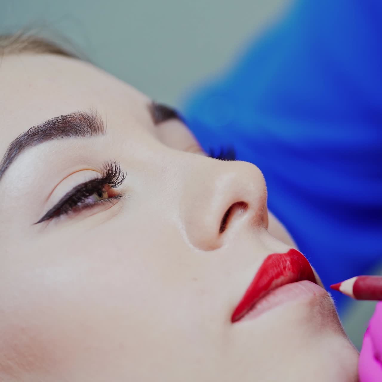 Face of a beautiful woman in a beauty salon. Cosmetologist painting client's lips with a red pencil before the permanent make-up. Close-up.