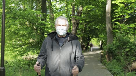 Active-senior-old-man-in-mask-training-Nordic-walking-in-park-during-quarantine