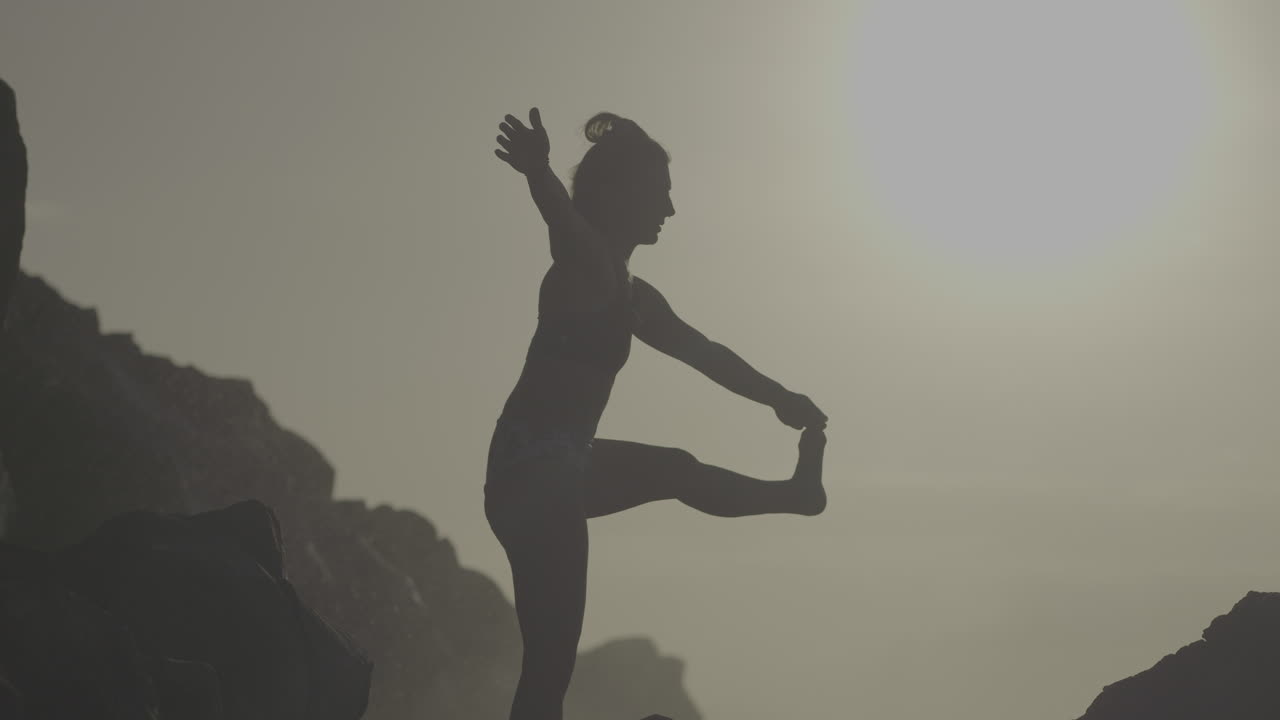 Woman practicing yoga on rocks at sunrise