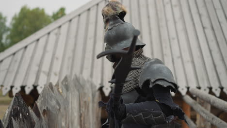 knight in dark armor walks heavily along fence holding spear