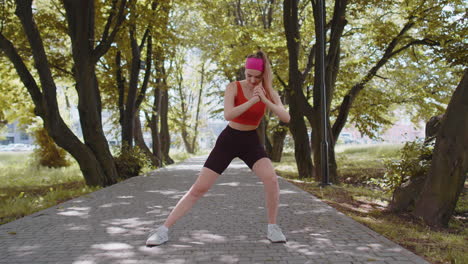 atleta en forma delgada chica deportiva haciendo sentadillas, escuchando música en auriculares, pérdida de peso aeróbica en el parque