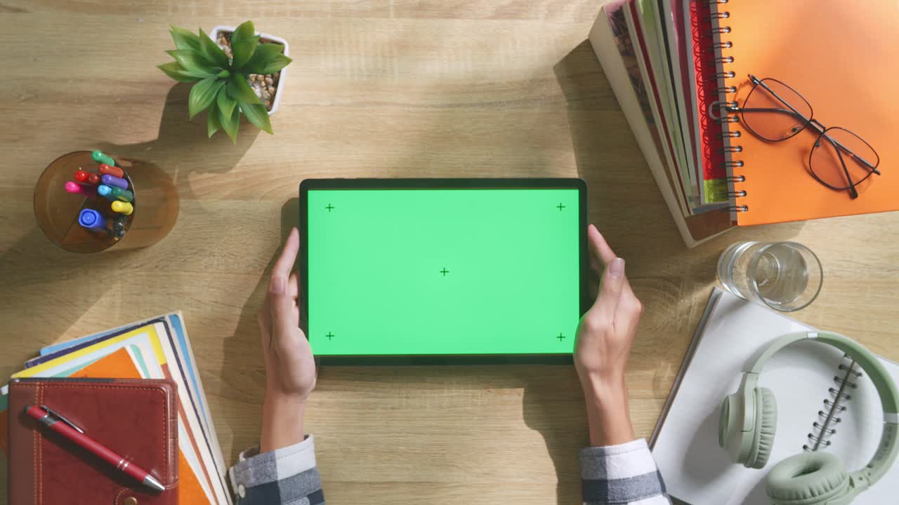 vista de arriba hacia abajo de una computadora portátil con pantalla verde simulada pantalla chromakey en un escritorio de oficina de madera al lado de la libreta con bolígrafos, gafas y un vaso de agua.