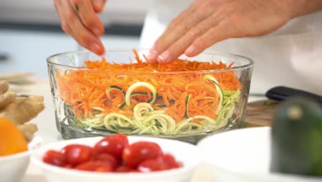 massaging bowl of shredded carrots and zoodles in bowl to make zucchini noodles adding to bowl healthy vegan vegetarian lifestyle diet detox tomatoes ginger