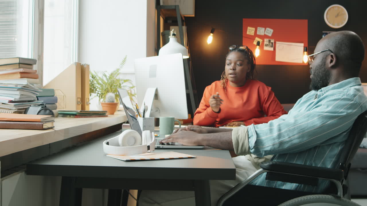 Man in Wheelchair Working on Laptop and Talking with Female Colleague