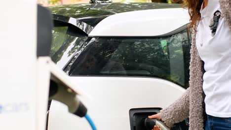 mujer cargando un coche eléctrico en la estación de carga 4k