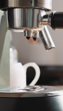 las gotas de bebida caen sobre la bandeja de la cafetera. una mujer joven sostiene una taza de cerámica de café listo cerca de la máquina de café. la comodidad de la rutina matutina