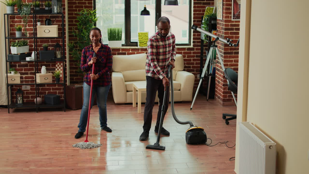 Young happy couple listening to music and washing floors in apartment