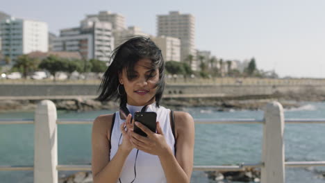 Retrato-De-Una-Joven-Hispana-En-La-Playa-Usando-Un-Teléfono-Inteligente-Explorando-Fotos-Disfrutando-De-Un-Día-Ventoso