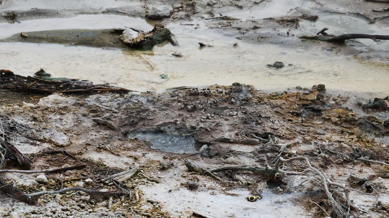 Panning shot of hot water of geothermal crater and flowing creek during daytime,close up