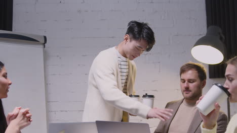 young man bringing takeaway coffee to his colleagues during a team meeting