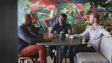 four male creative colleagues talking at a table in their workplace canteen, three quarter length